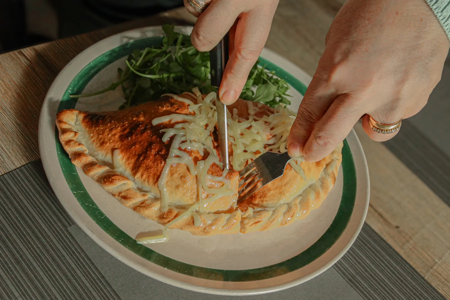 Een calzone die met mes en vork wordt aangesneden, met rucola ernaast