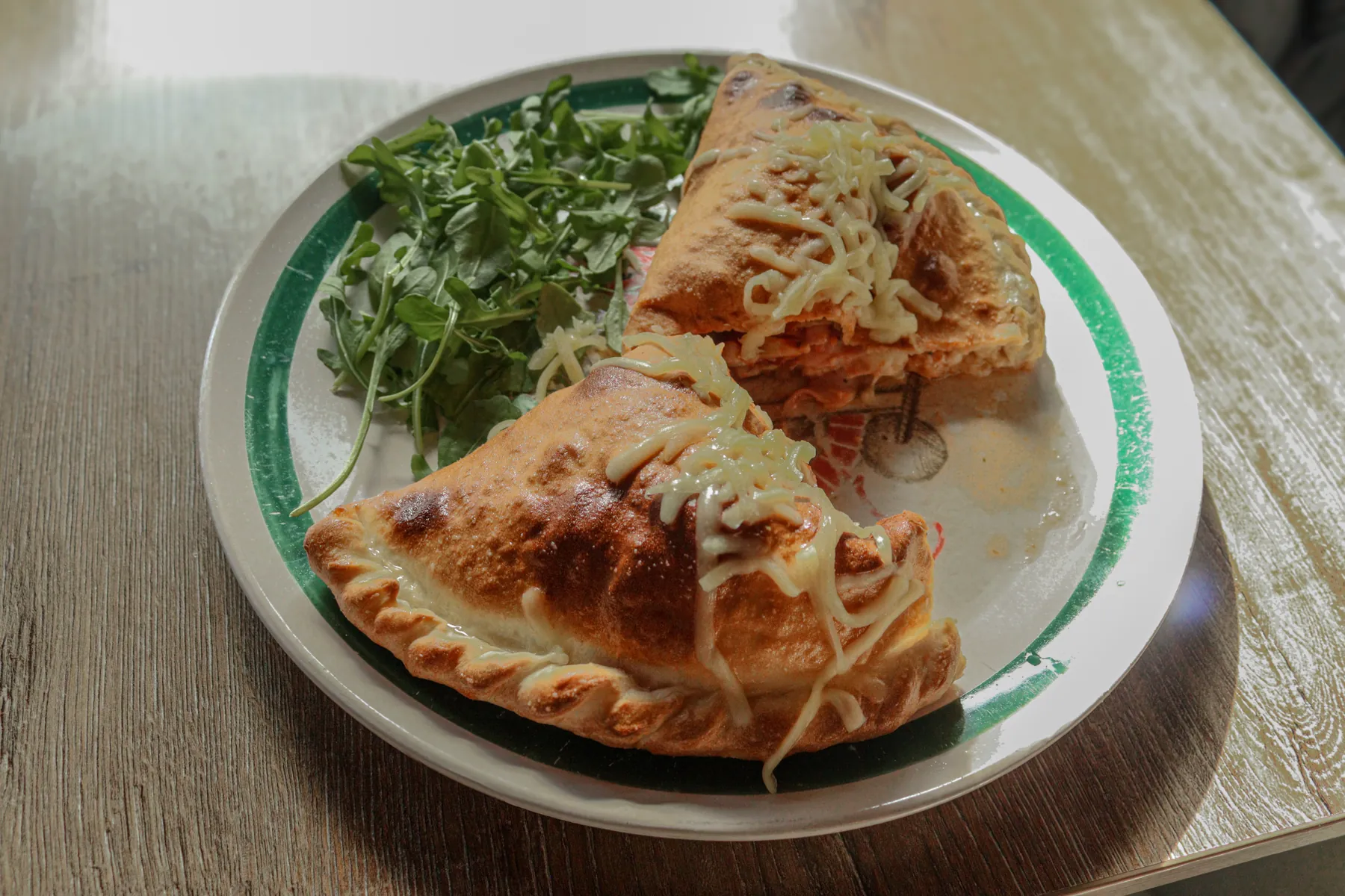 Een calzone in twee helften op een bord met rucola