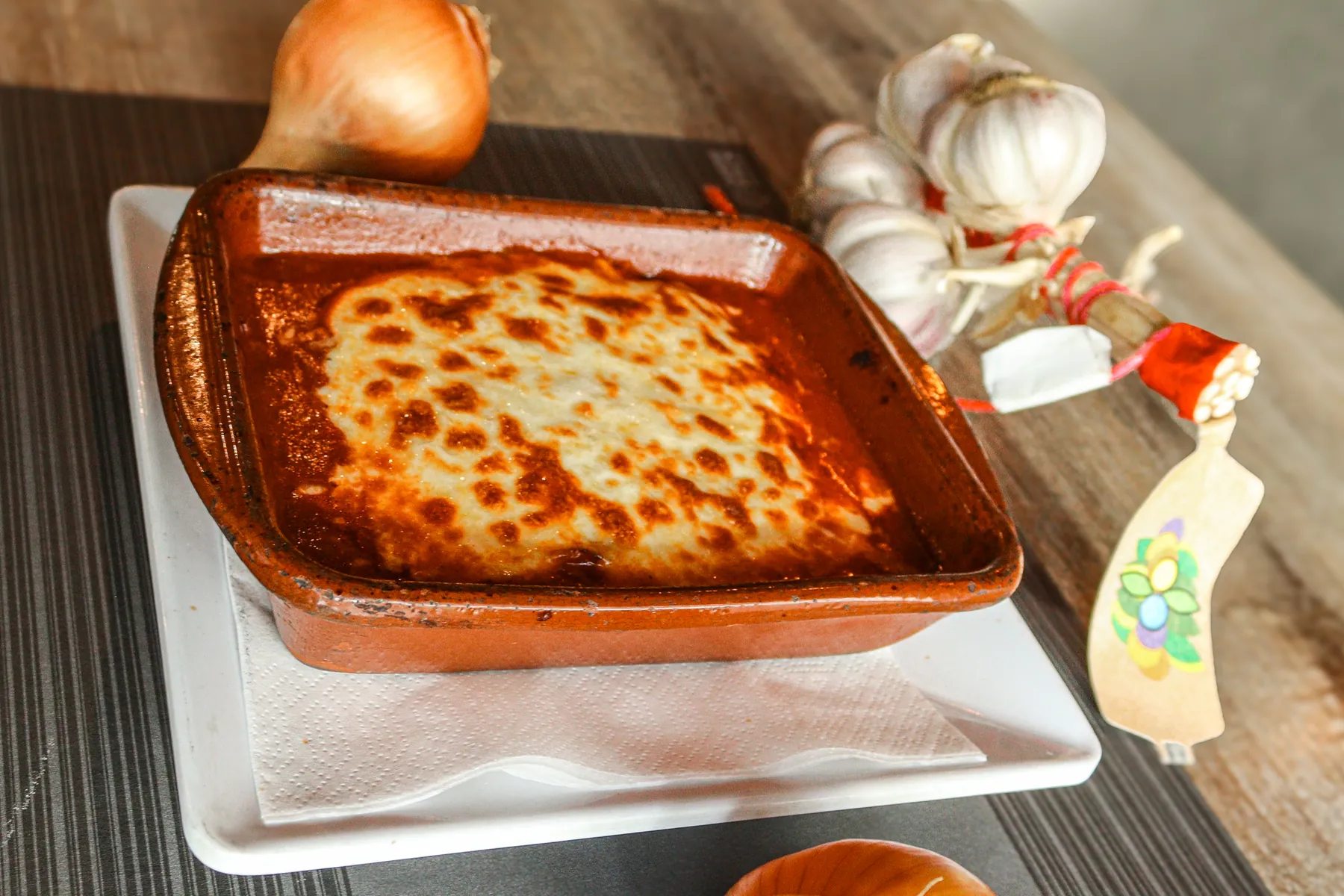 Lasagne in een terracotta ovenschaal, met knoflook ernaast