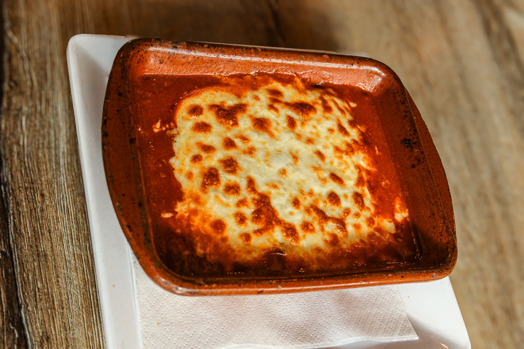 Lasagne al forno, goudbruin gegratineerd in een terracotta schaal