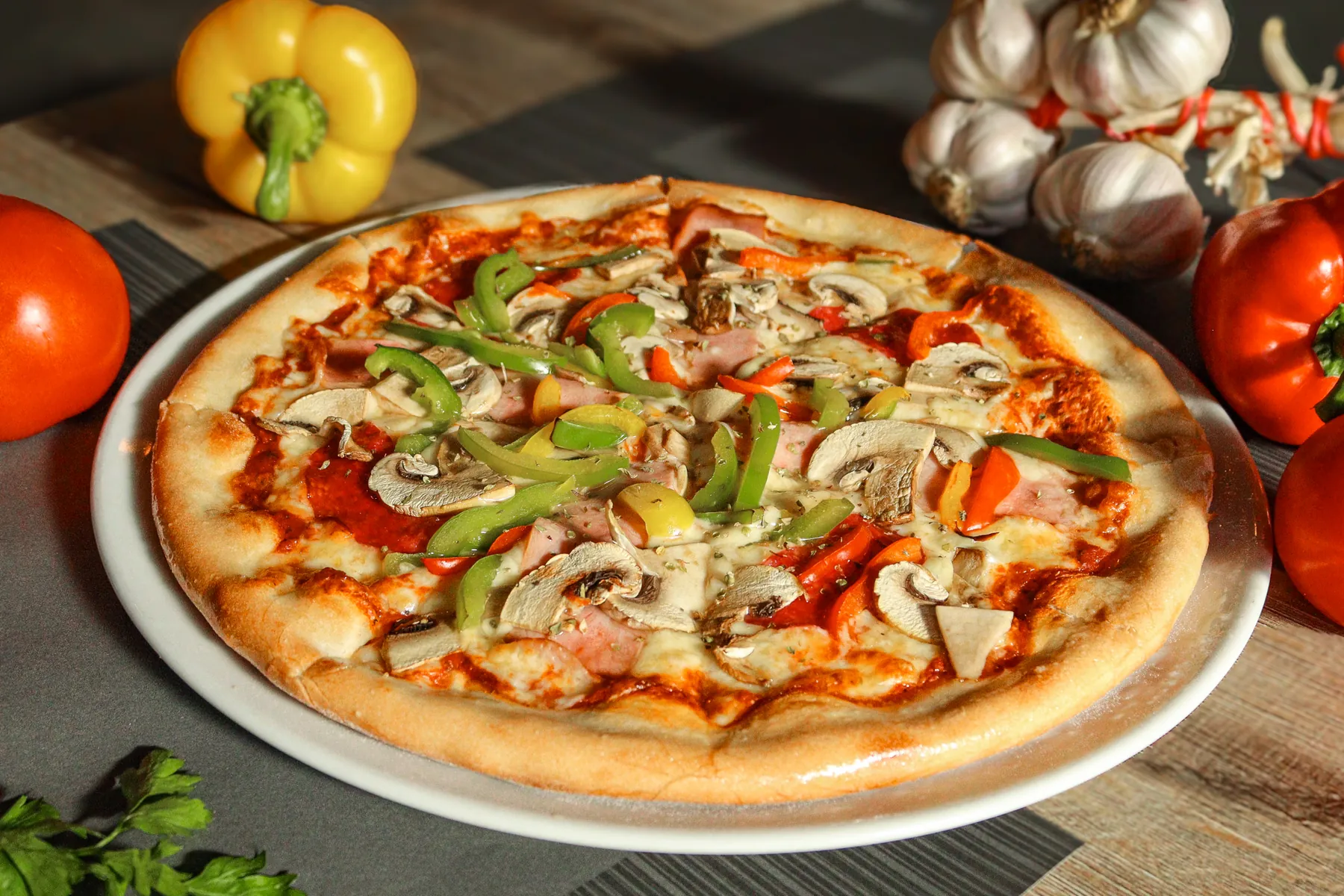 Een pizza met groenten, omringd door verse tomaten, knoflook en paprika