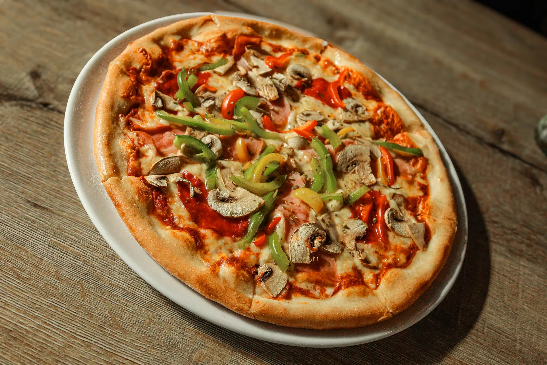 Een pizza met parmaham, paprika en champignons op een houten tafel