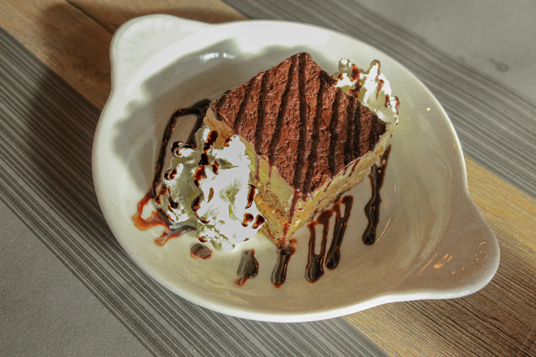 Een punt huisgemaakte tiramisu met chocoladesaus in een schelpvormig schaaltje