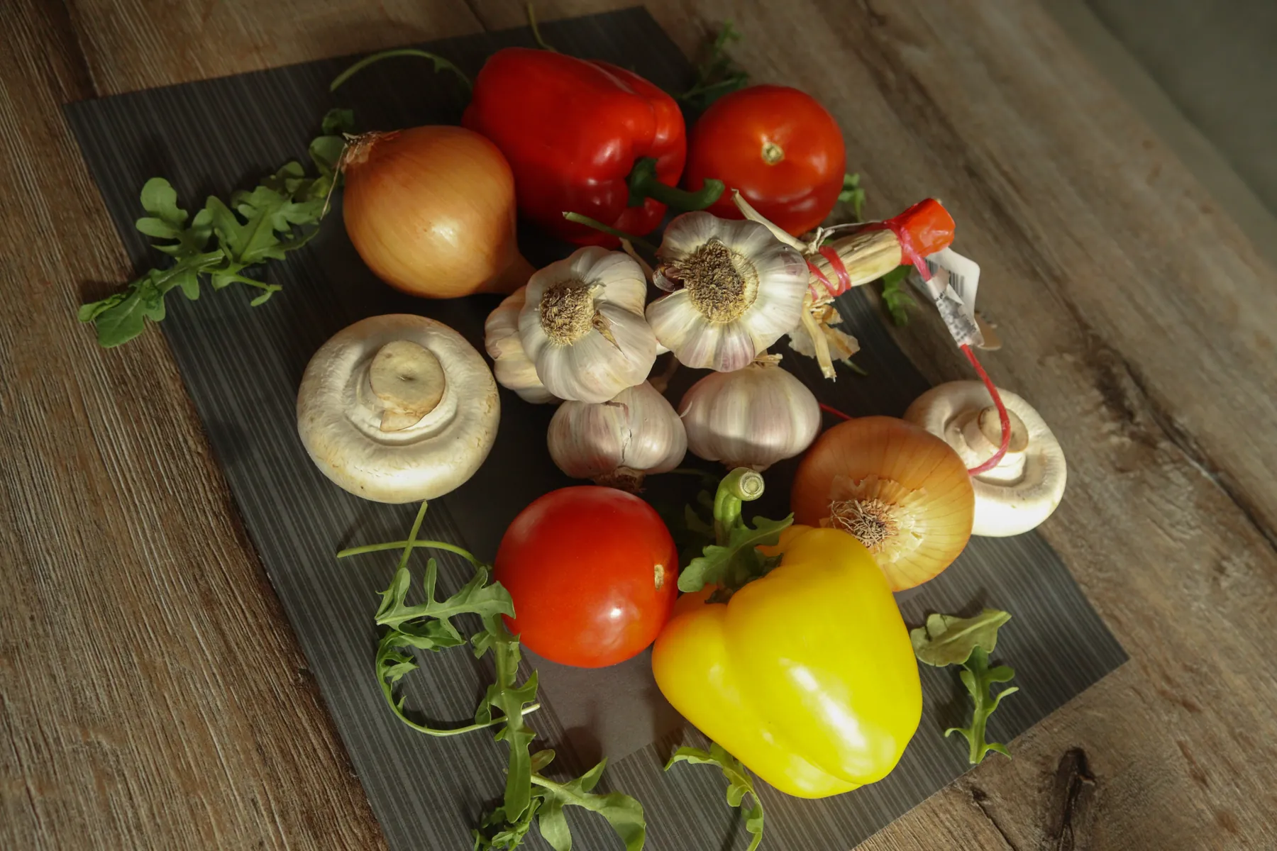 Verse tomaten, knoflook, uien, paprika en champignons op een donkere plank