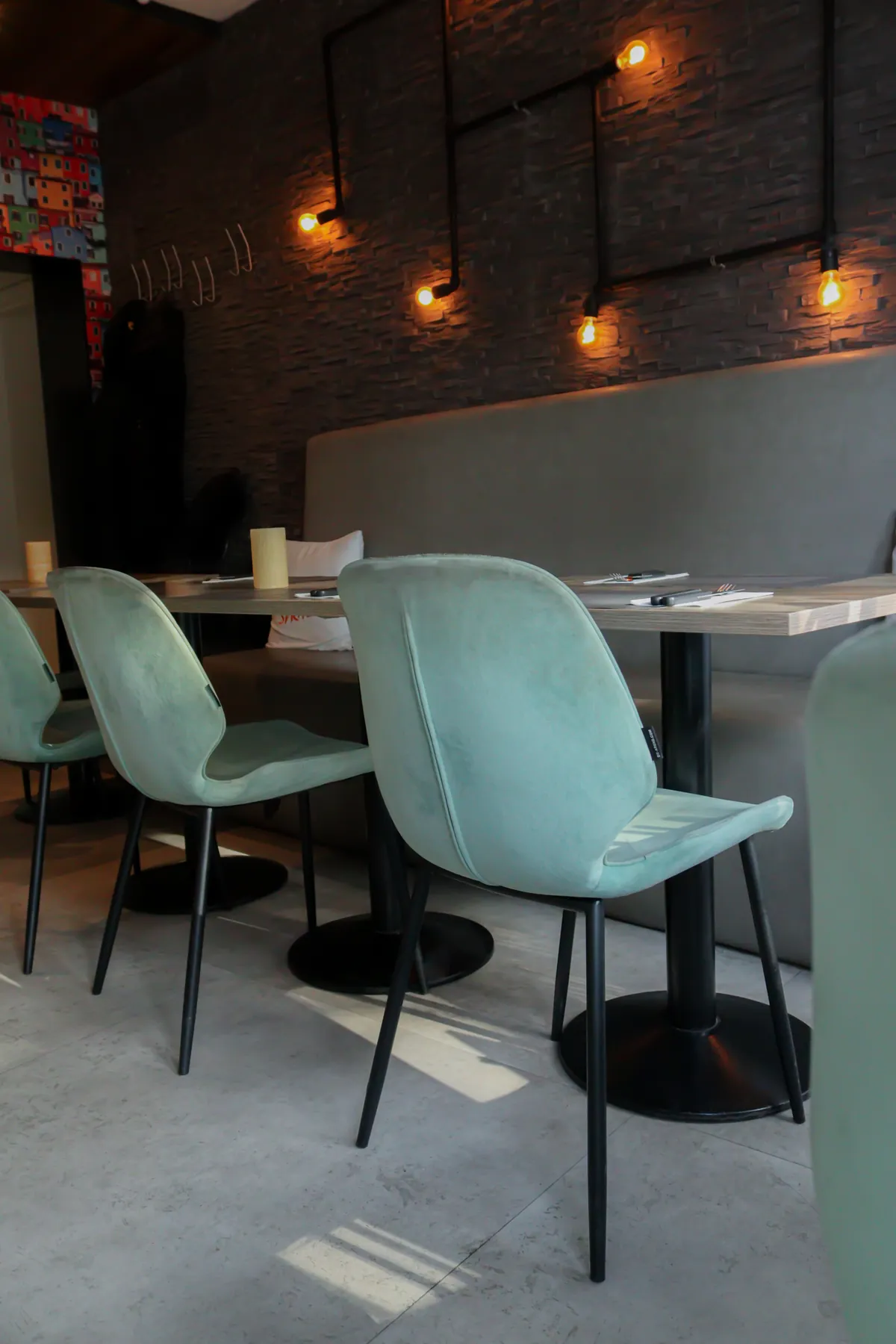 Tafels met mintgroene stoelen onder een lichtsnoer langs de bakstenen wand