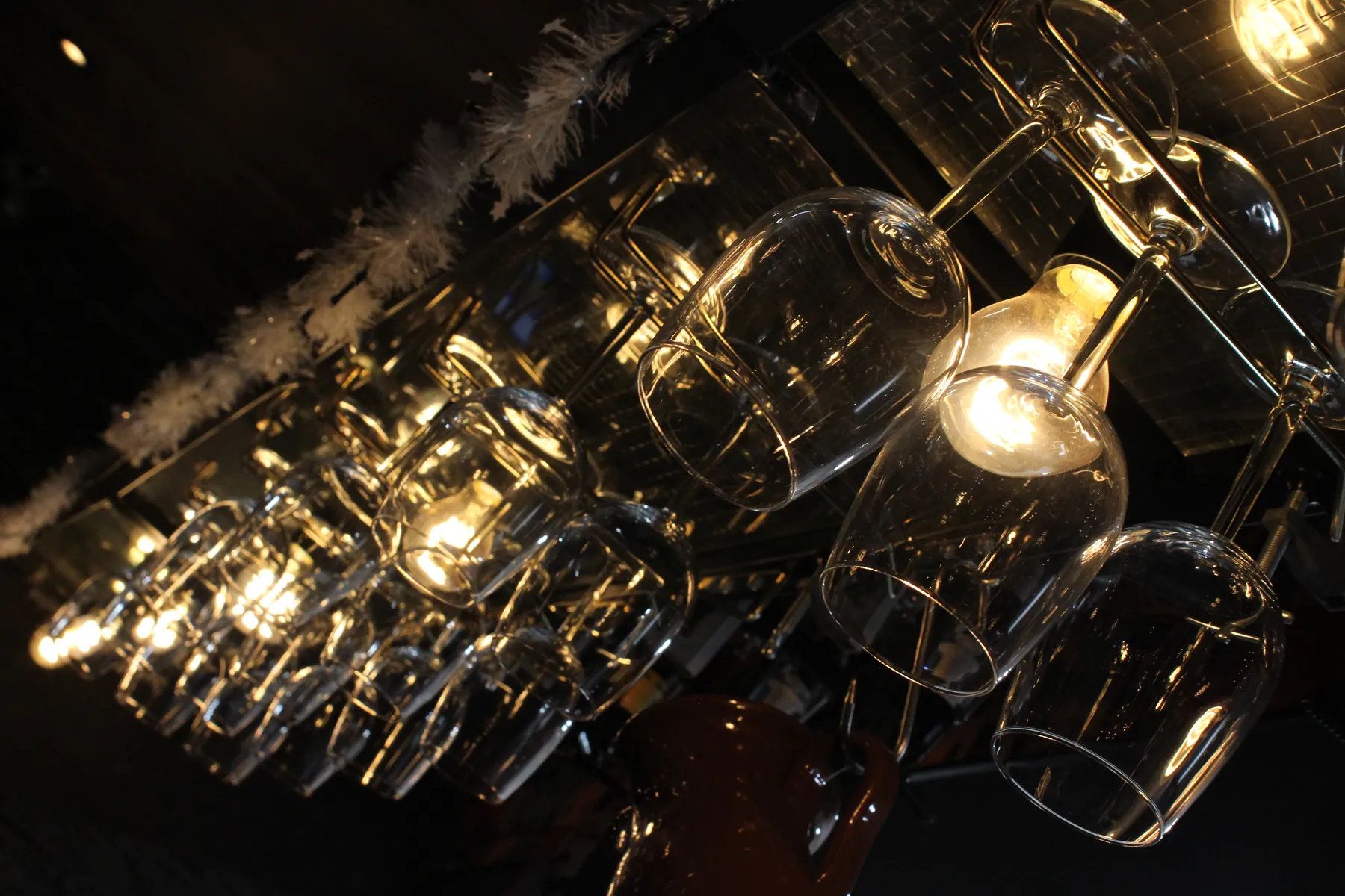Wijnglazen die ondersteboven boven de bar hangen, in het licht van een gloeilamp